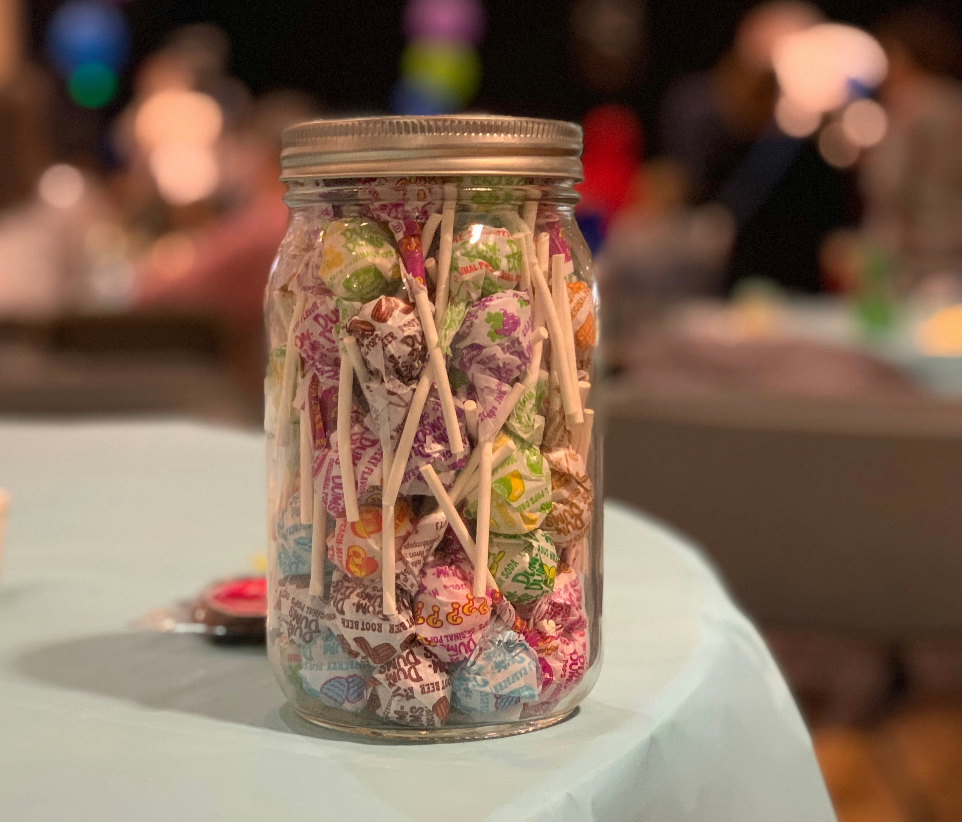A mason jar full of suckers sits on a table display.