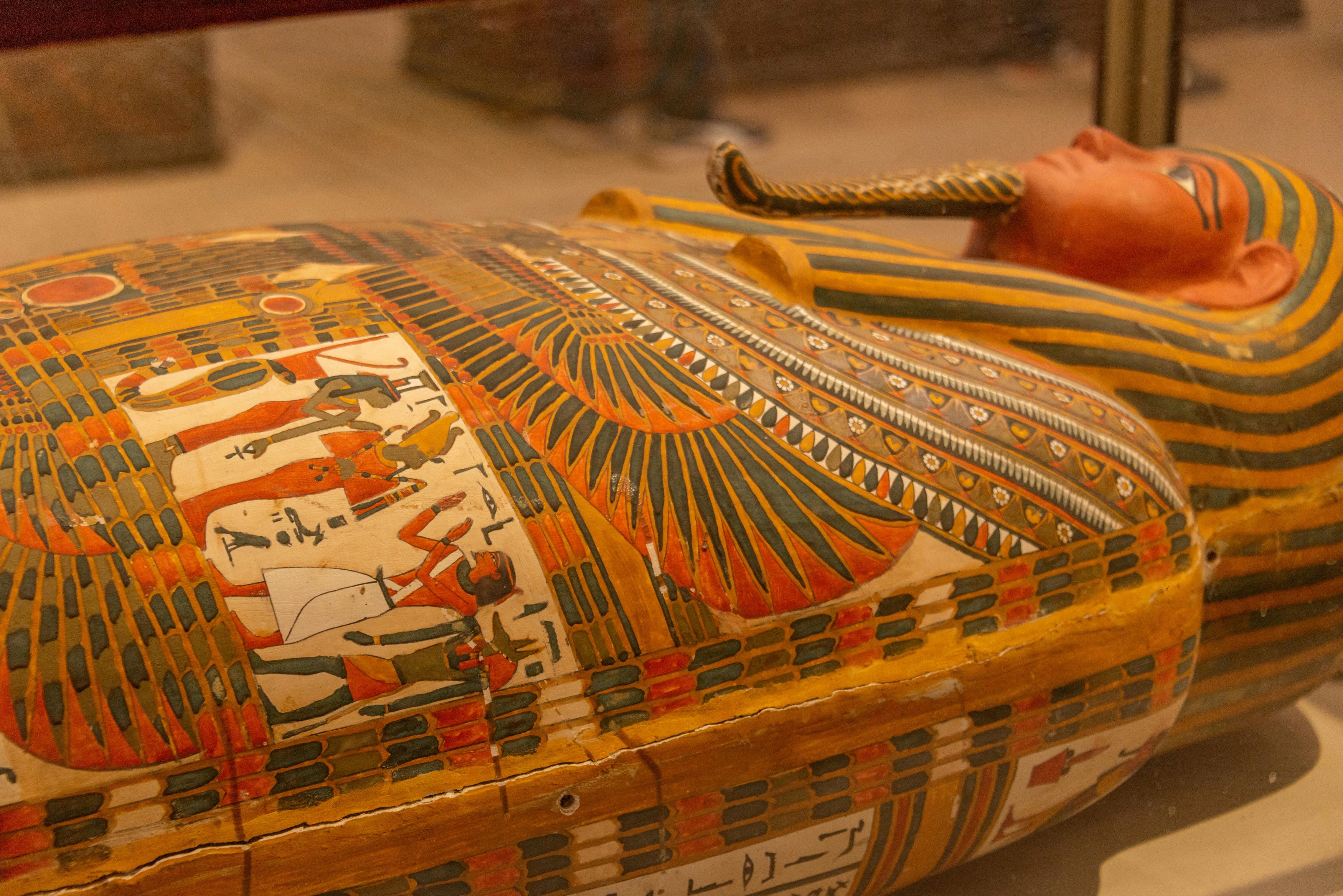 An Egyptian mummy covered in heiroglyphics lies in a glass case inside a museum.