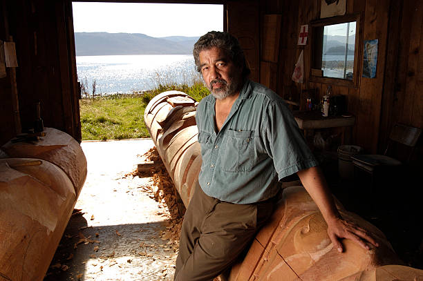 A Haida Gwaii man stands beside a totem pole he carved.